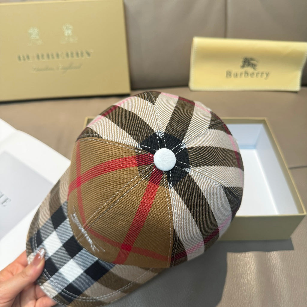 Burberry plaid cap with circular top button detail in tan, red, and black.