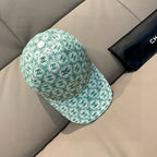 Chanel cap, mint green repeating CC logo print, curved brim, side view on box.