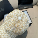 Beige baseball cap with gold monogram pattern and light-colored top button at crown center.