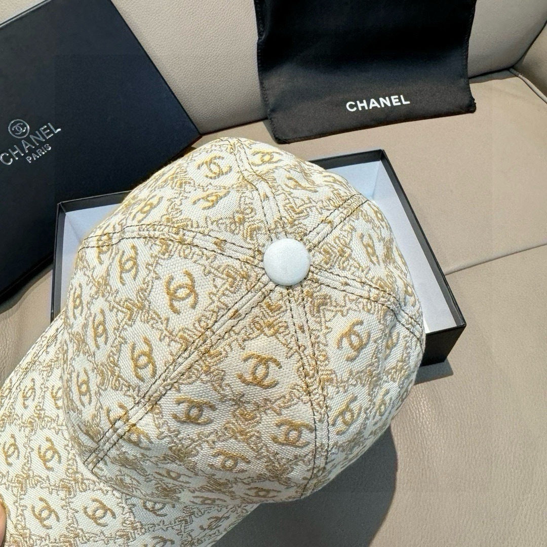 Beige baseball cap with gold monogram pattern and light-colored top button at crown center.