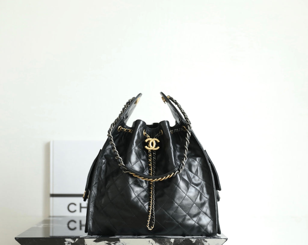 Black Chanel bag with quilted leather, chain handles, and gold CC logo at top