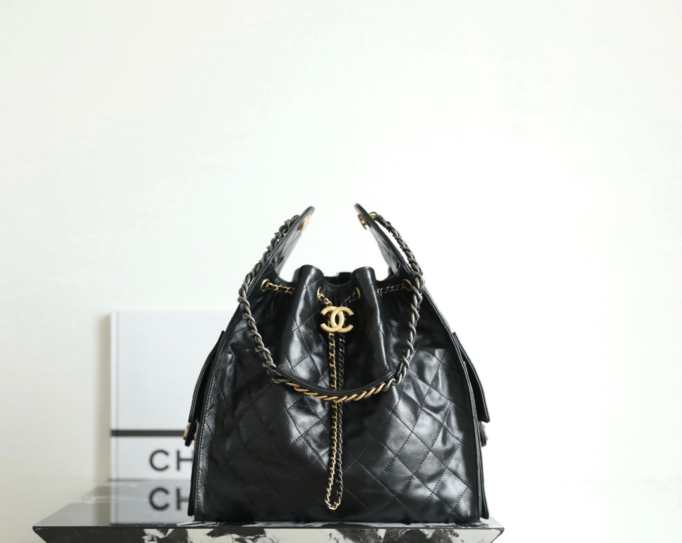 Black Chanel bag with quilted leather, chain handles, and gold CC logo at top