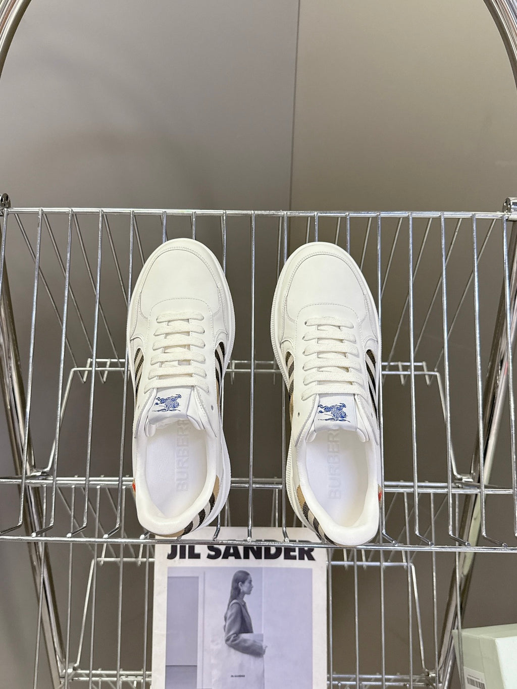 White low-top sneakers on metal rack, with blue logo on tongue and lace-up front