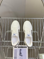 White low-top sneakers on metal rack, with blue logo on tongue and lace-up front