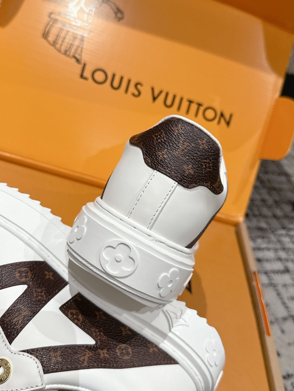 White sneaker heel with brown monogram-style cap and embossed flower details