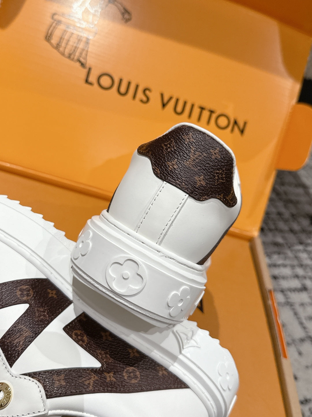 White sneaker heel with brown monogram-style cap and embossed flower details