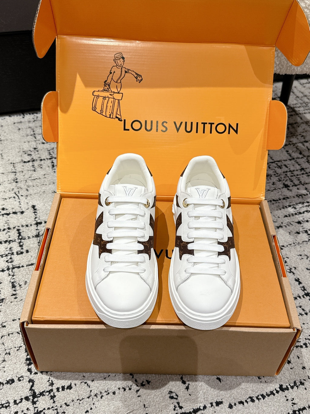 White low-top sneakers with brown monogram-style side panels and white laces