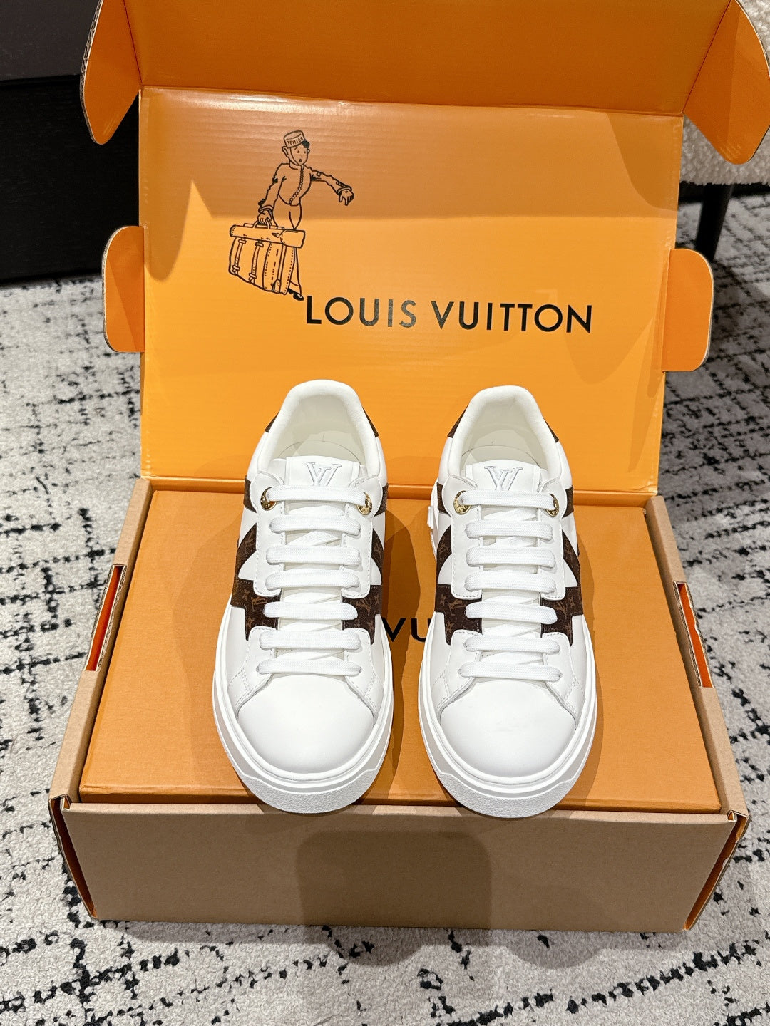 White low-top sneakers with brown monogram-style side panels and white laces