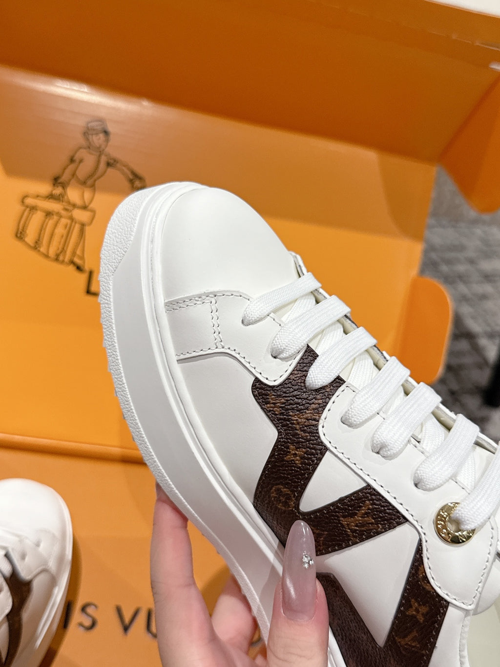 Close-up: white lace-up sneaker with brown panel and gold logo detail