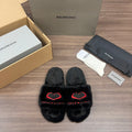 Black plush slide sandals with red heart-style logo detail, crossover front