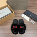 Black plush slide sandals with red heart-style logo detail, crossover front
