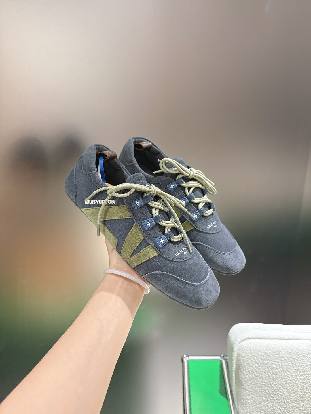 Blue-gray lace-up sneaker held up, with green geometric side patch and light laces