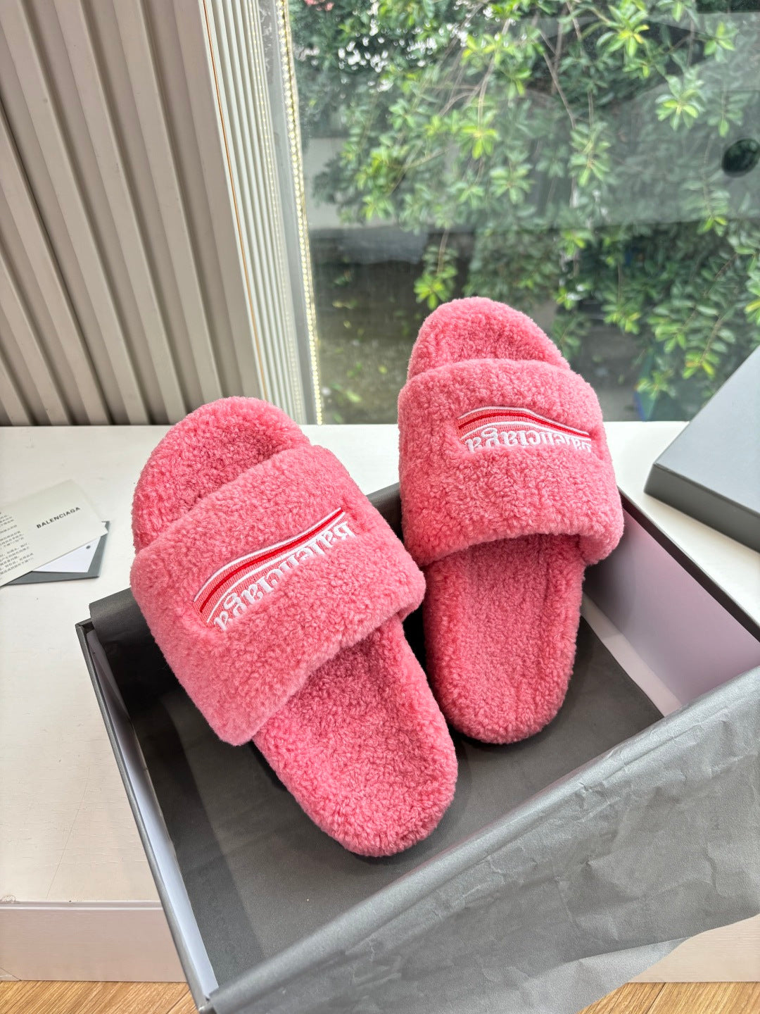 Balenciaga fuzzy pink slide sandals with logo strap, angled side view on box