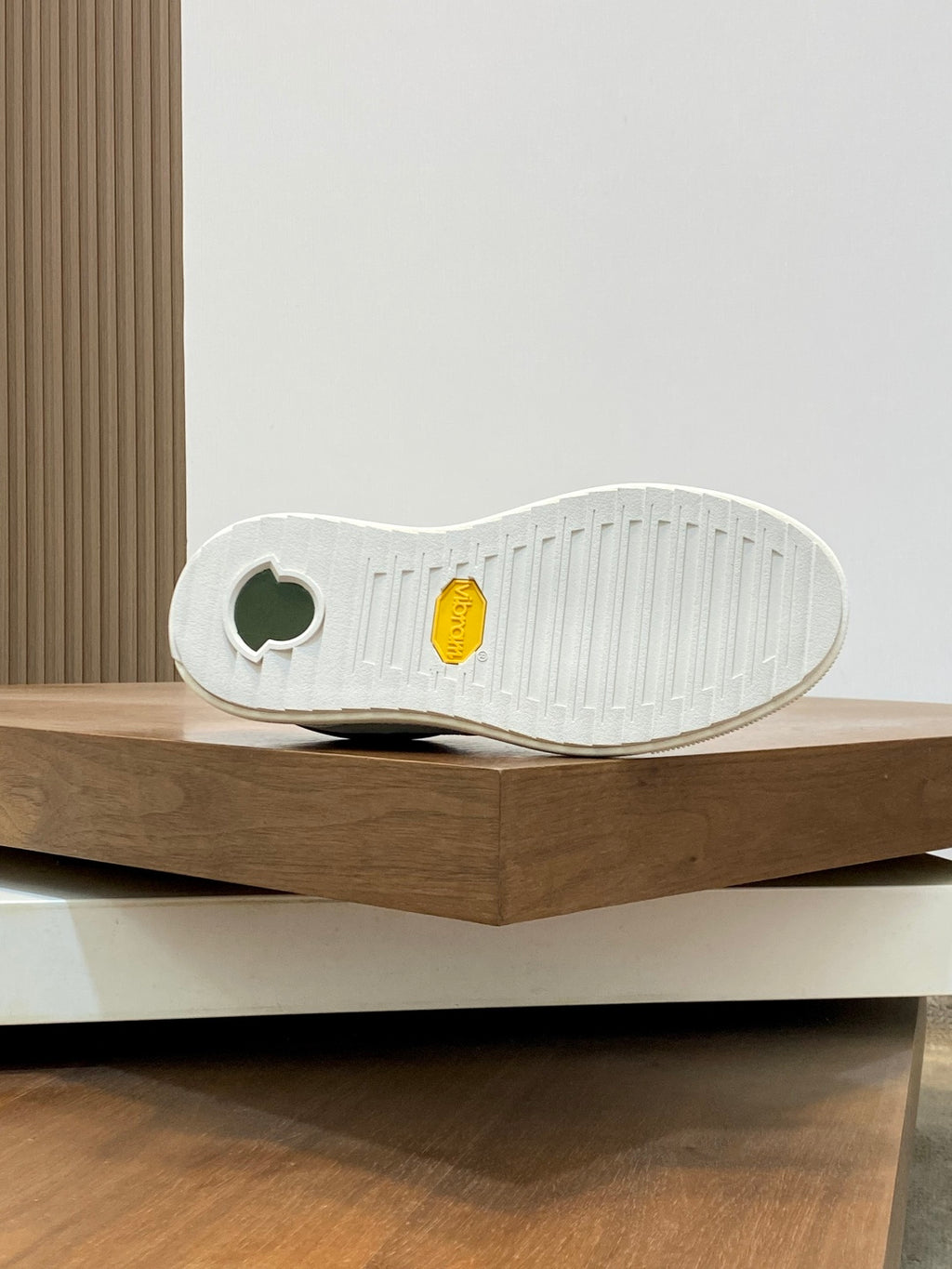 Sneaker outsole view: white tread with round logo detail and yellow patch