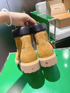 Tan lace-up boots with dark heel collar and embossed pattern, held in hand