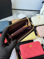 Small quilted zip wallet opened to show dark interior lining and dual zipper compartments.