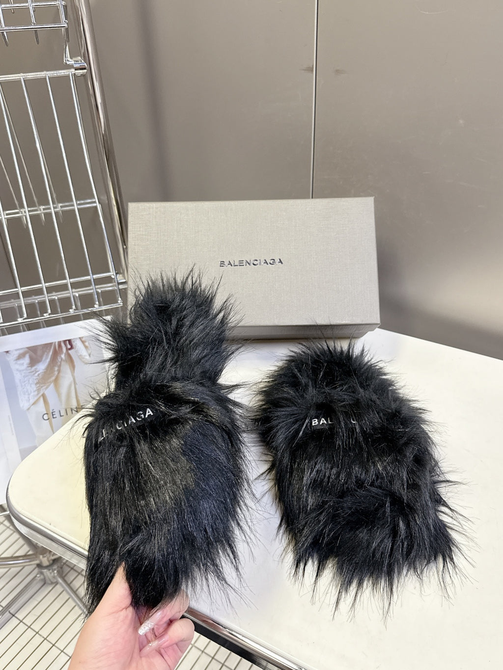 Black fuzzy slide sandals held in hand, wide straps with Balenciaga logo
