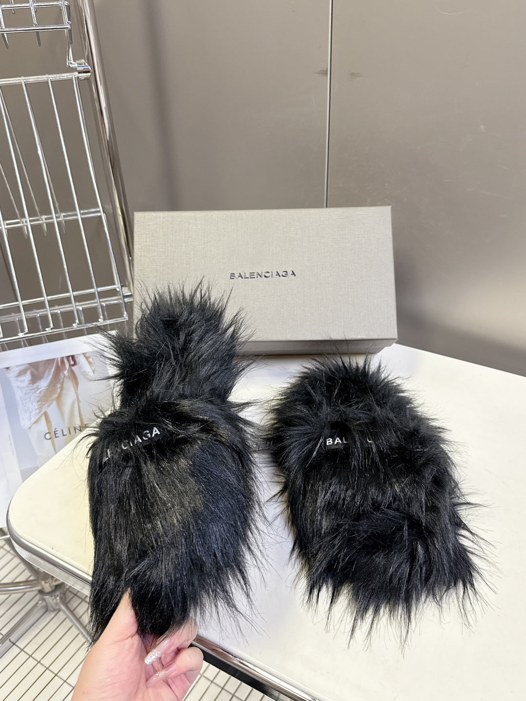 Black fuzzy slide sandals held in hand, wide straps with Balenciaga logo