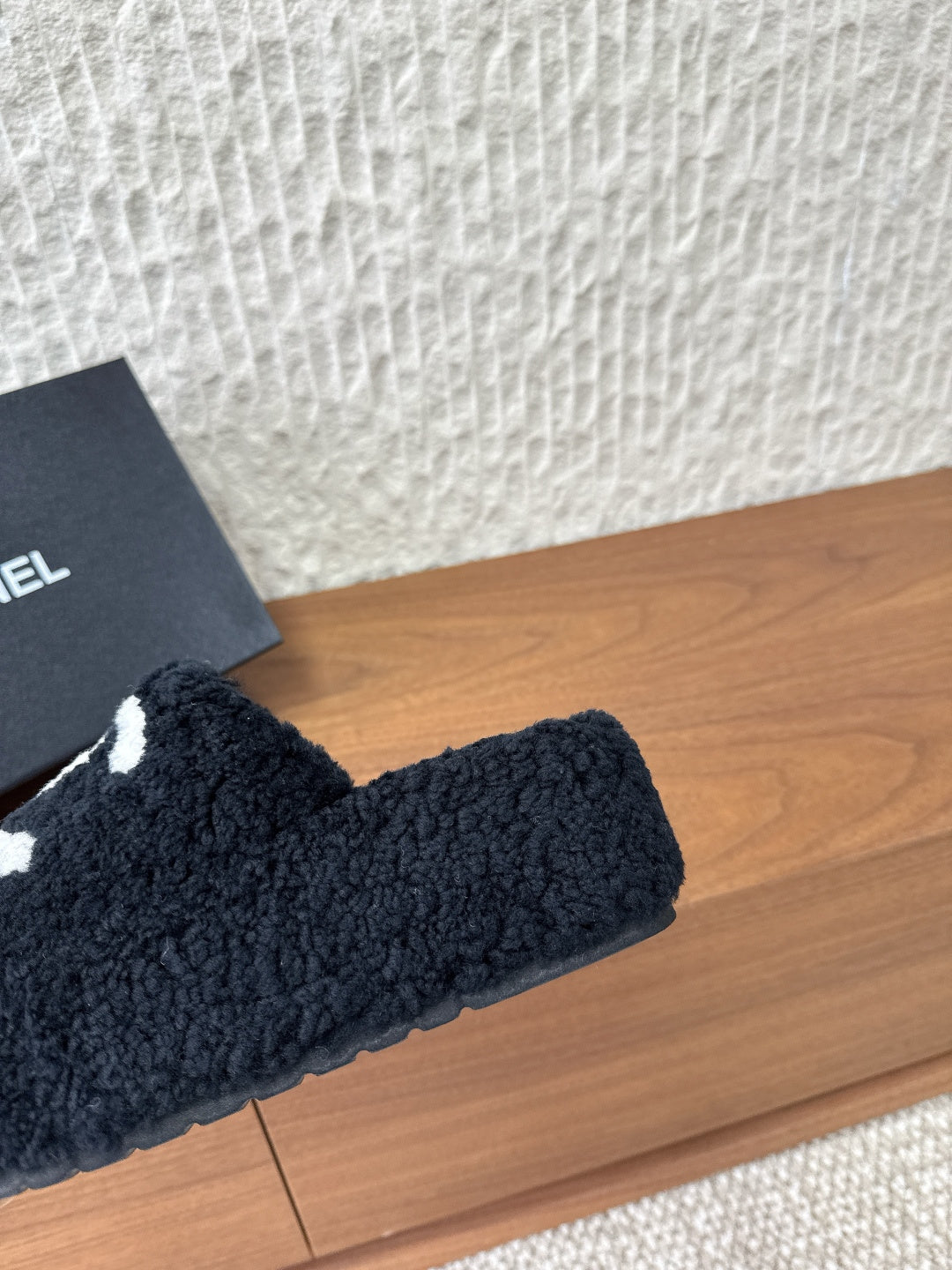 Black plush slide sandal with oversized white logo mark on strap