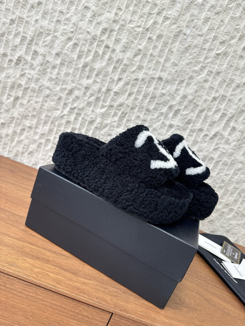 Black plush slide sandals with white logo strap, laid on a box