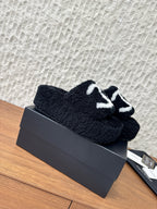 Black plush slide sandals with white logo strap, laid on a box