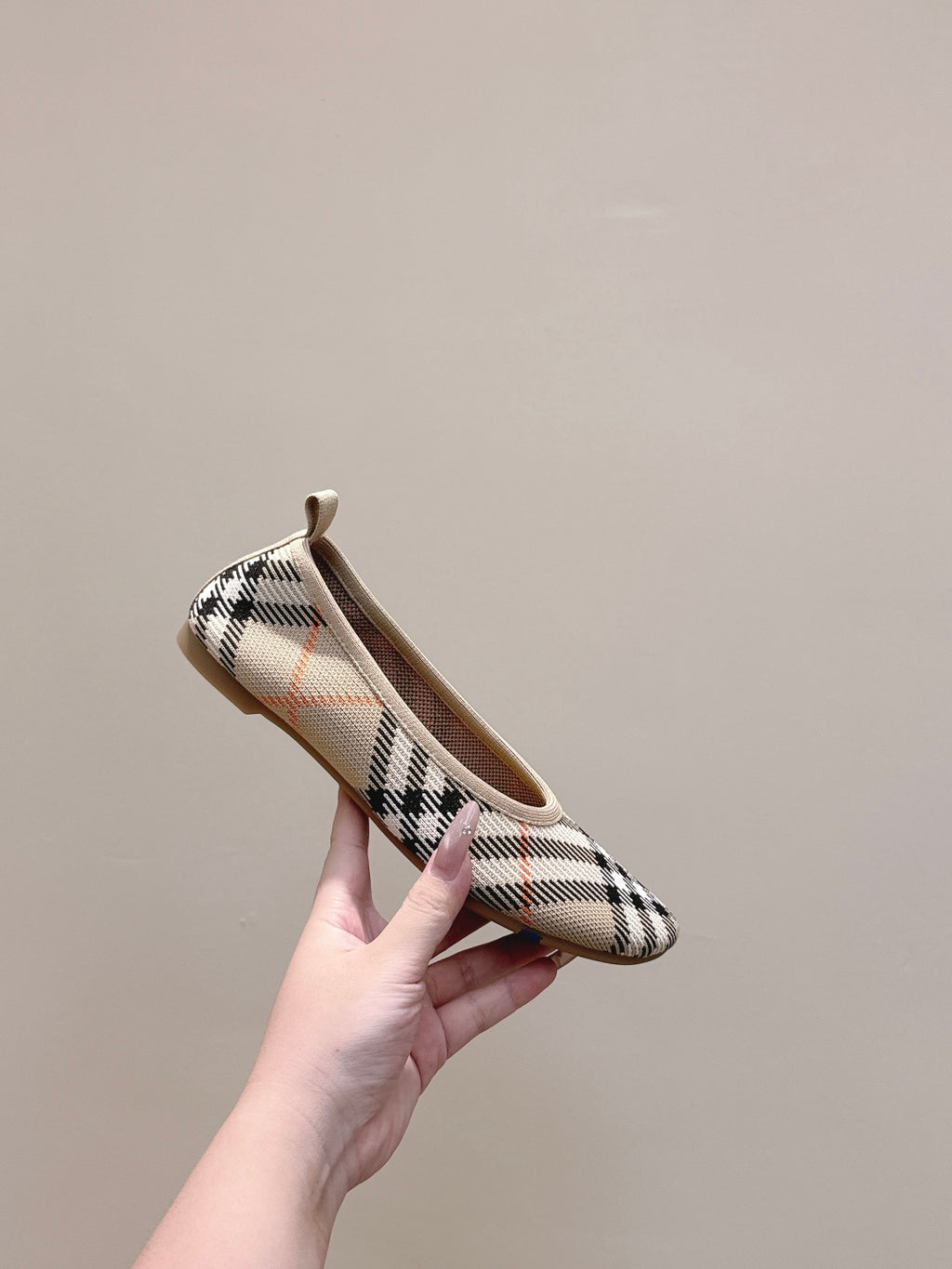 Plaid slip-on shoe held up by hand, showing rounded toe and heel loop