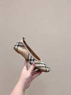 Plaid slip-on shoe held up by hand, showing rounded toe and heel loop