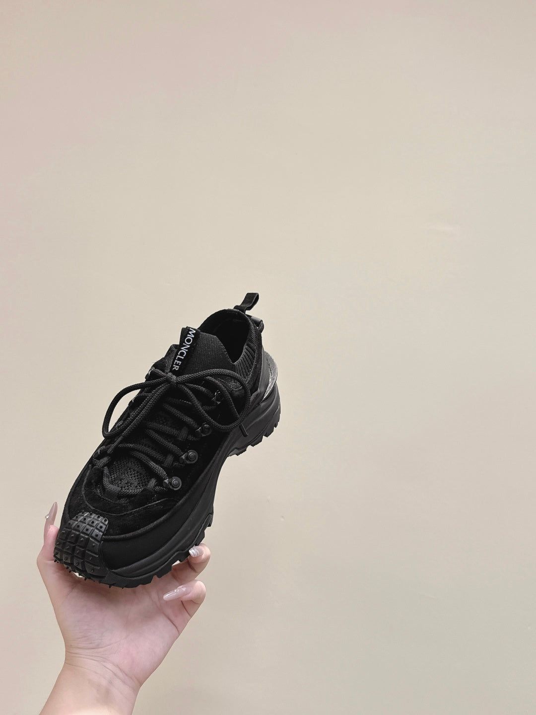 Black Moncler lace-up sneaker held in hand, front-angled view