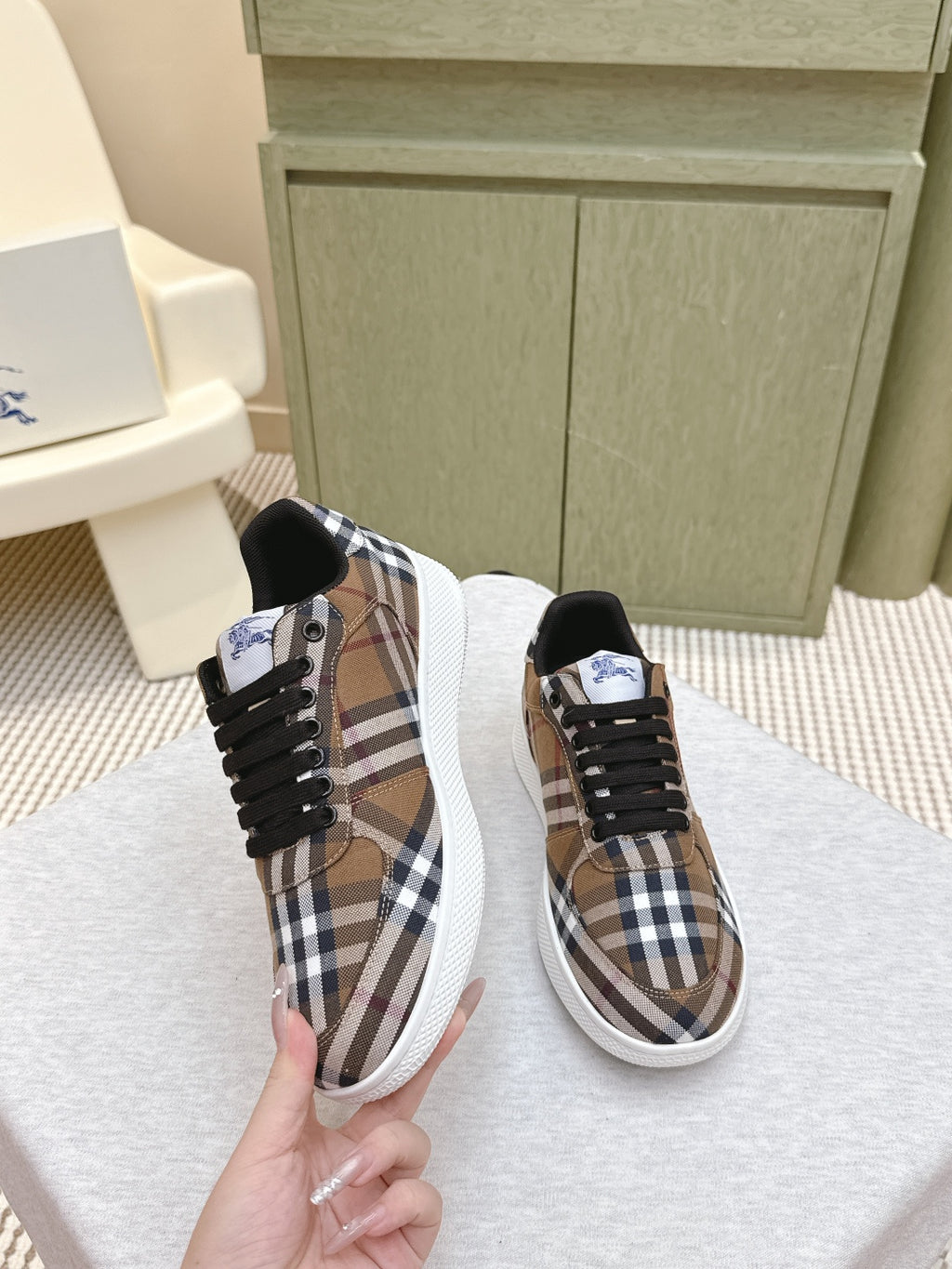 Burberry sneakers held by hand, brown plaid upper with black laces and white sole