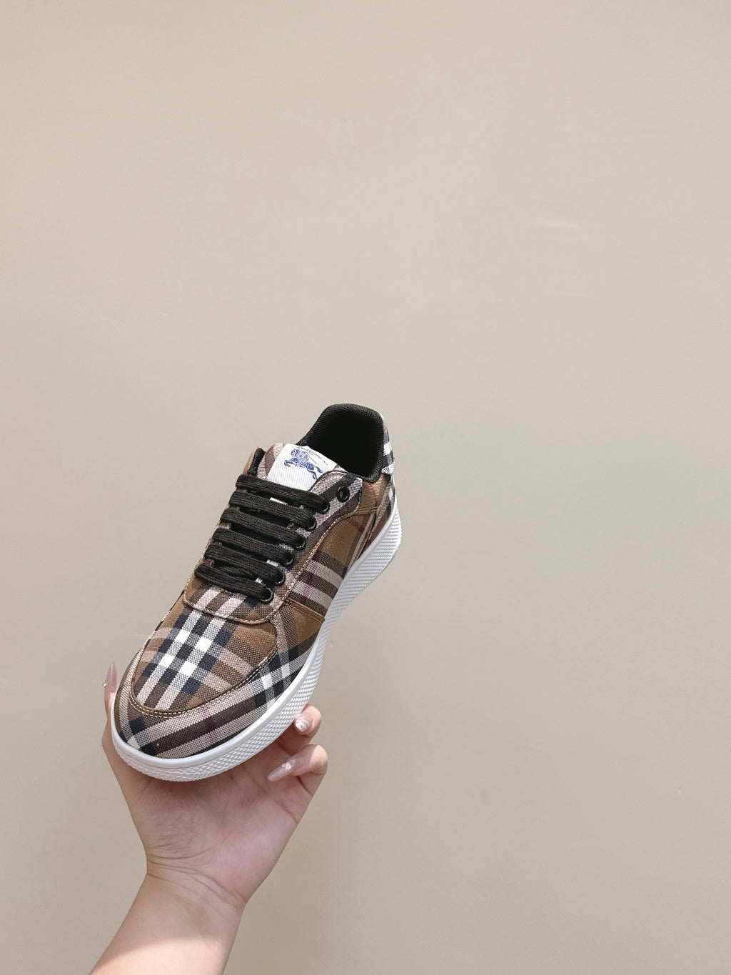 Burberry sneaker in hand, brown plaid upper with black laces and white rubber sole