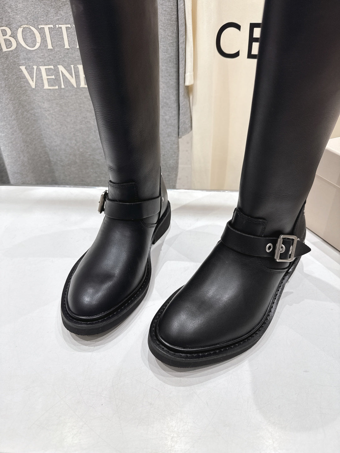 Close-up of two black tall boots with side buckle strap and stacked sole
