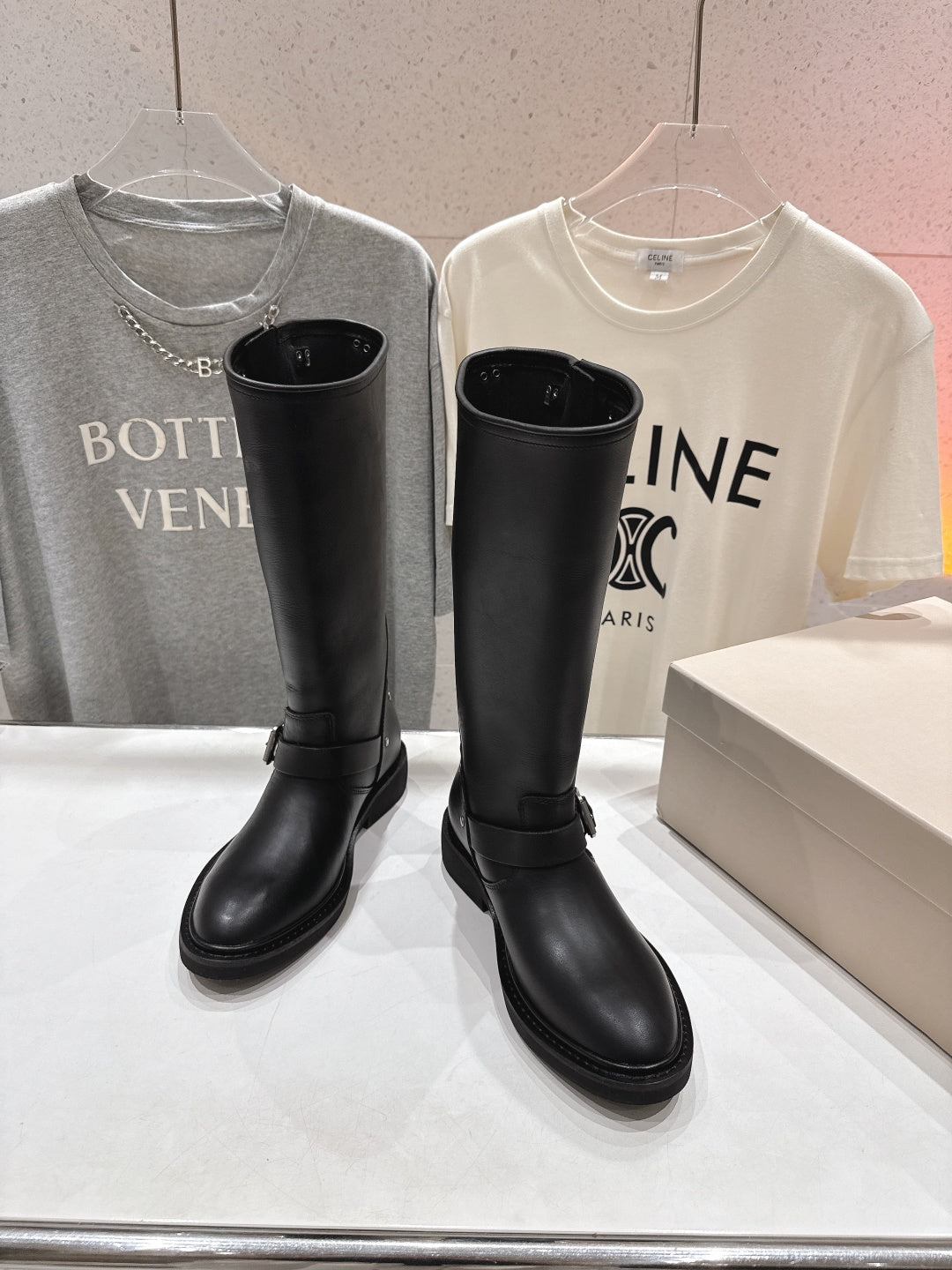 Pair of black tall boots standing side by side, with strap and buckle detail