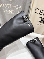 Black tall boots with metal buckle strap; angled close-up on shelf