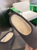 Close-up of dark gray suede slide sandals showing cream shearling interior