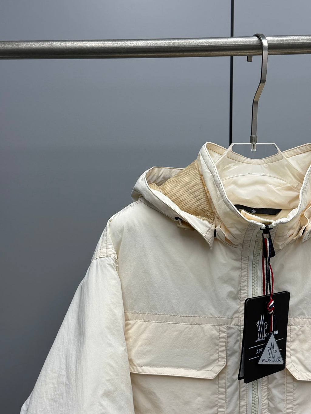 Light beige hooded jacket with front zipper, patch pocket, and Moncler emblem