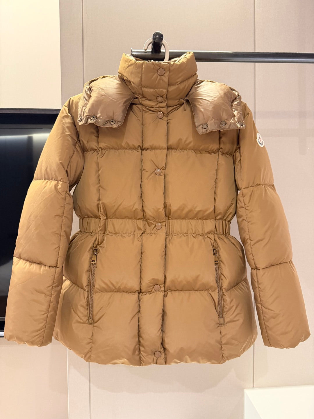 Long beige puffer jacket with hood, front zip, and side pockets