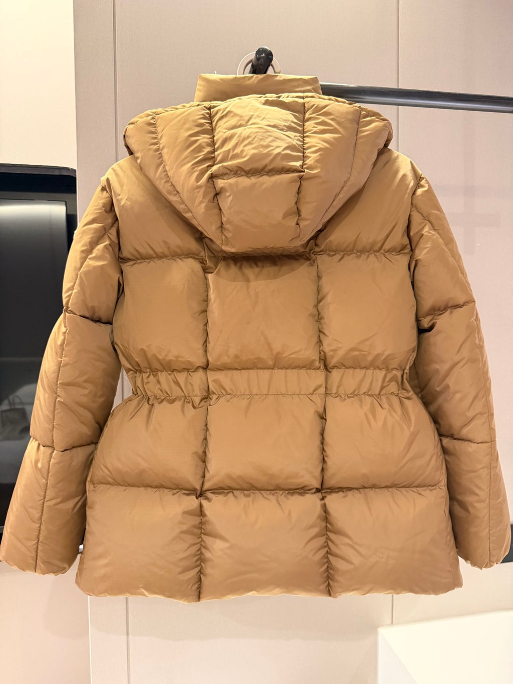 Long beige puffer jacket with hood, back quilting, and cinched waist