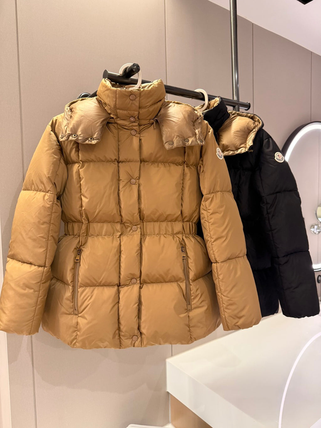 Long beige puffer jacket with hood, front zip, and quilted panels