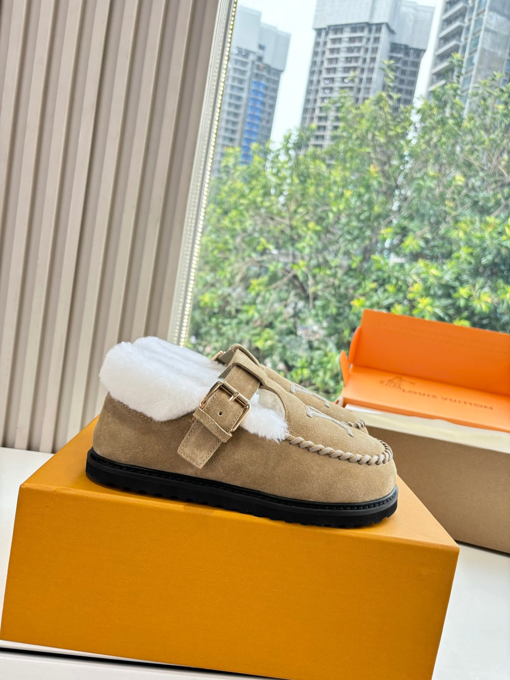 Tan suede shearling-lined loafer with buckle strap and Louis Vuitton monogram on box.