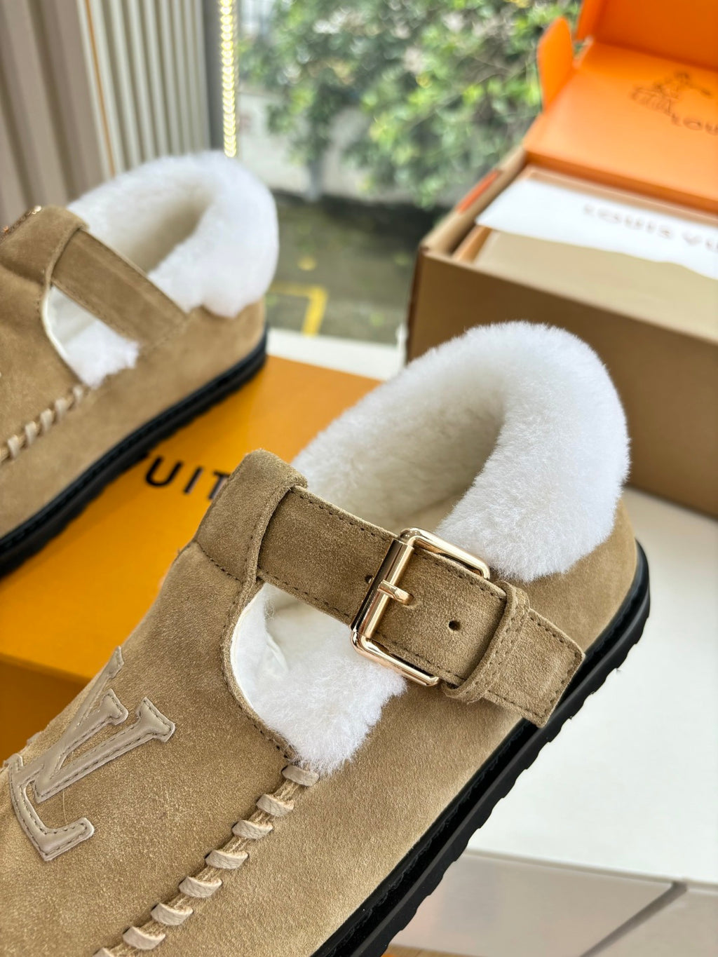 Tan suede shearling moccasin loafer close-up with buckle strap and Louis Vuitton monogram.