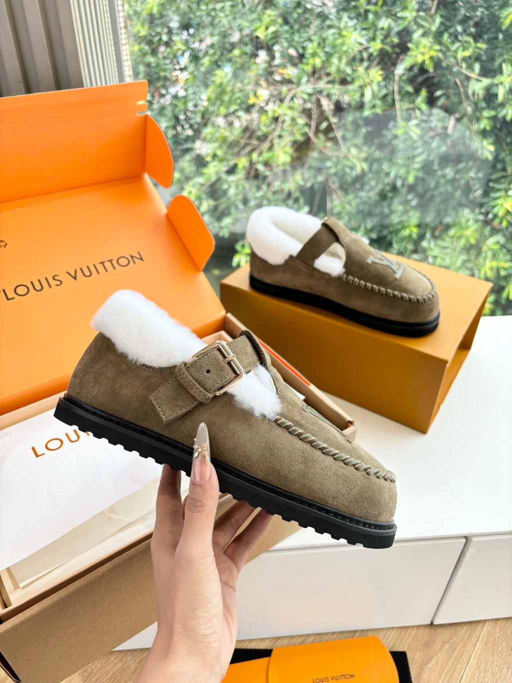 Taupe suede moccasin with white shearling lining, buckle strap, and thick rubber sole