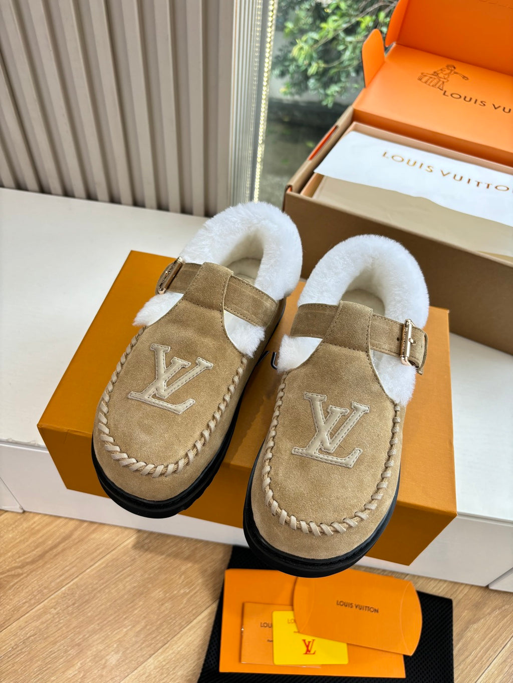Tan suede shearling moccasin loafers, front view with buckle strap and monogram.