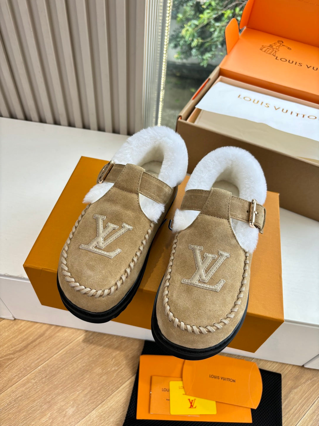 Tan suede shearling moccasin loafers, front view with buckle strap and monogram.
