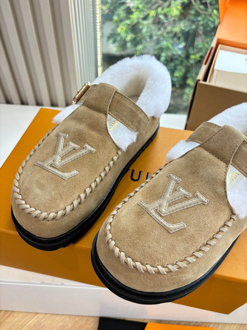Tan suede shearling moccasin loafers with buckle straps and Louis Vuitton monograms.