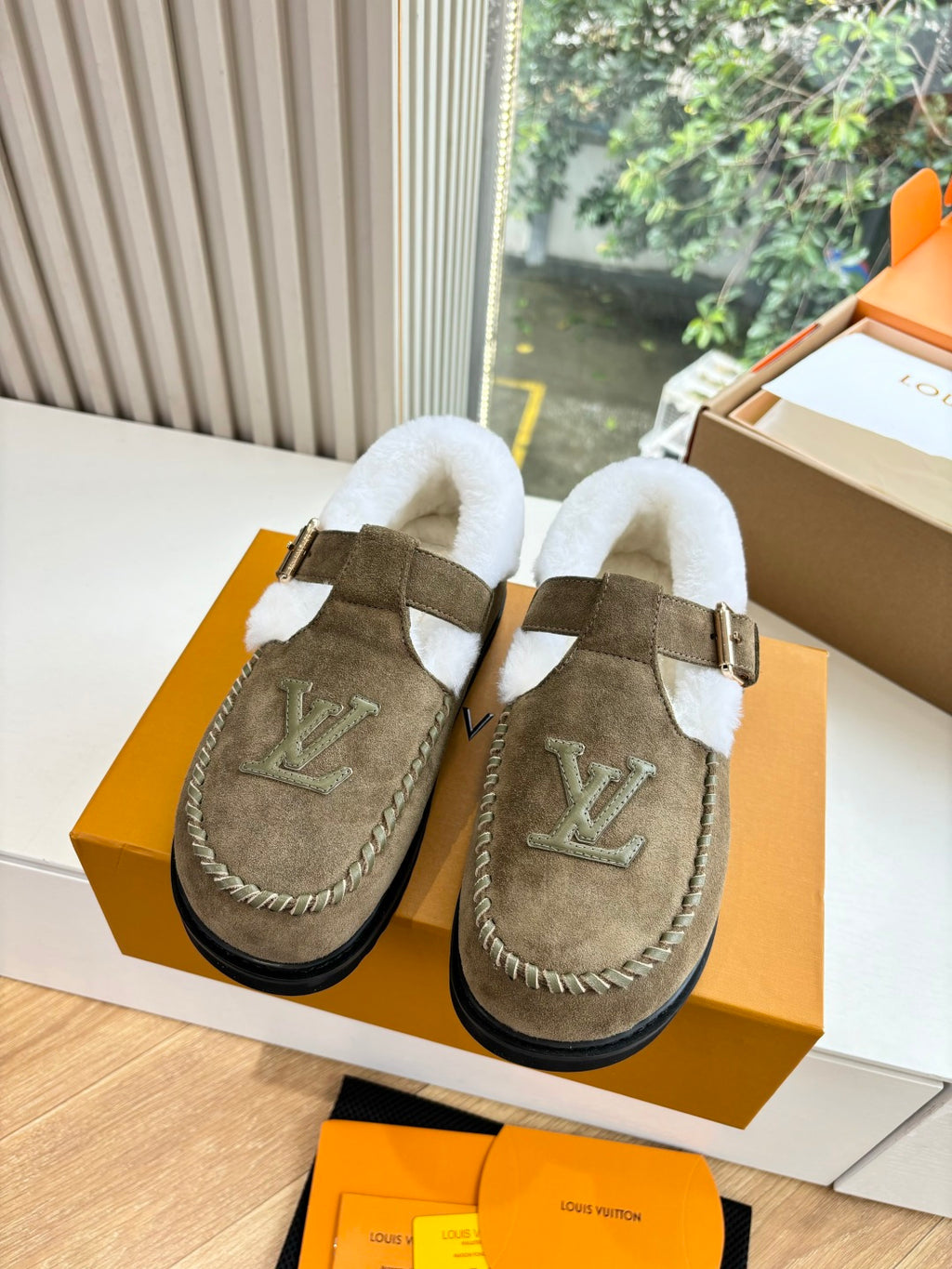 Pair of taupe suede moccasin shoes with white shearling lining and LV logo