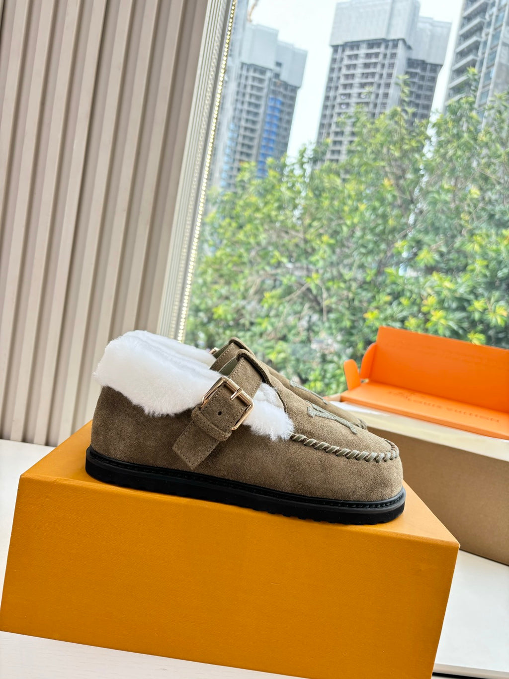 Taupe suede moccasin shoe with white shearling collar and buckle strap on box
