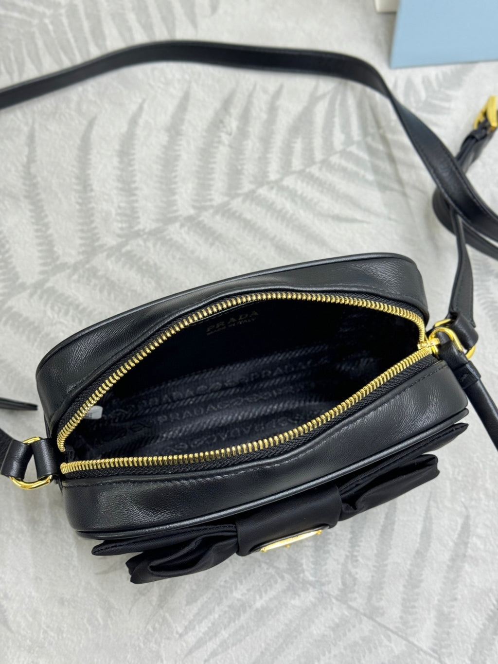 Prada crossbody bag side view with open zipper, black leather and gold trim