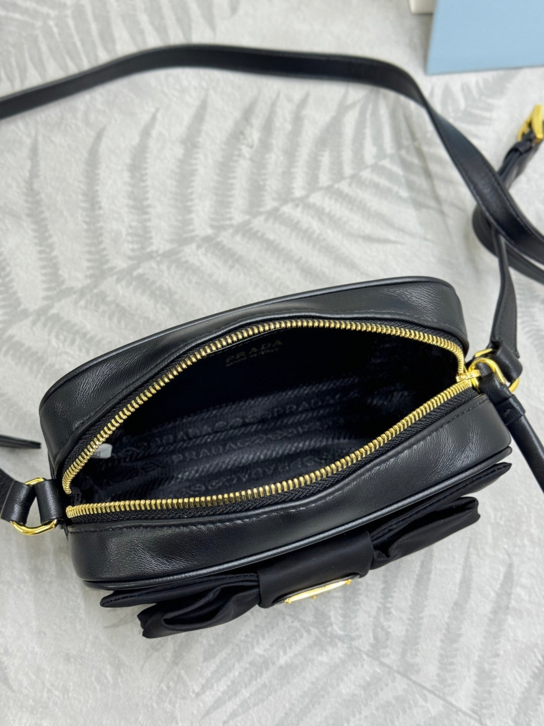 Prada crossbody bag side view with open zipper, black leather and gold trim