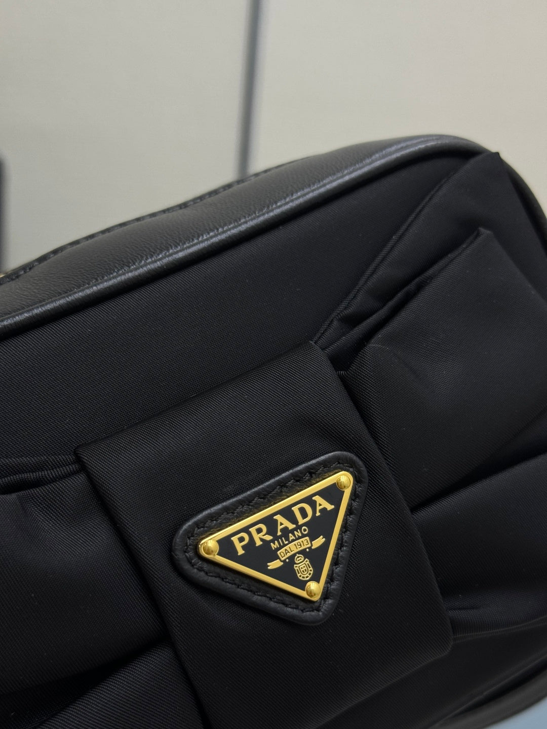 Prada bag close-up: black fabric with gold Prada triangular logo patch