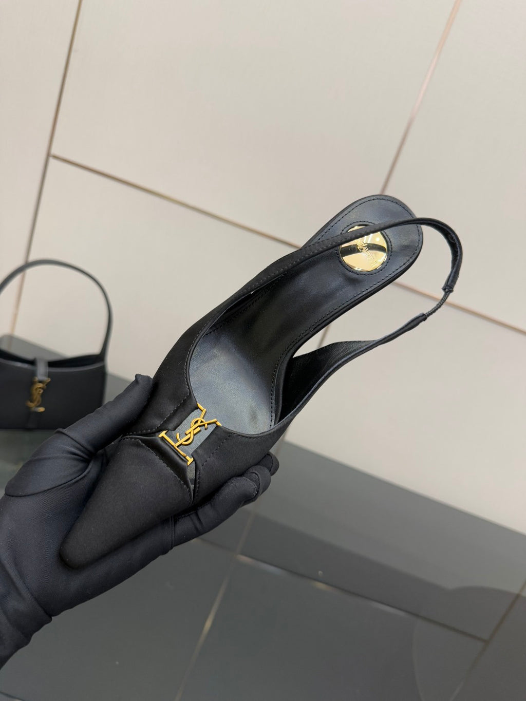 YSL black slingback pump held in gloved hand, close-up of strap and logo